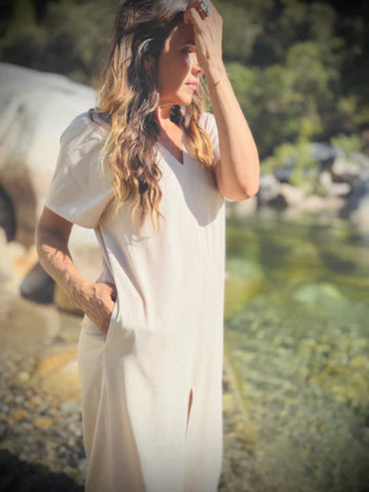 Woman in a white dress standing by a river with trees in the background